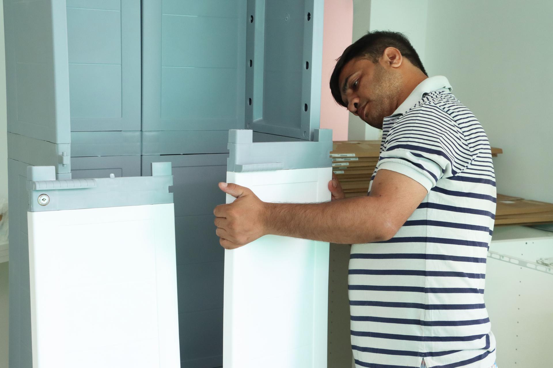 Image of man building modular furniture, assembling plastic storage unit, wardrobe setup in minimalist white and gray design, DIY home renovation