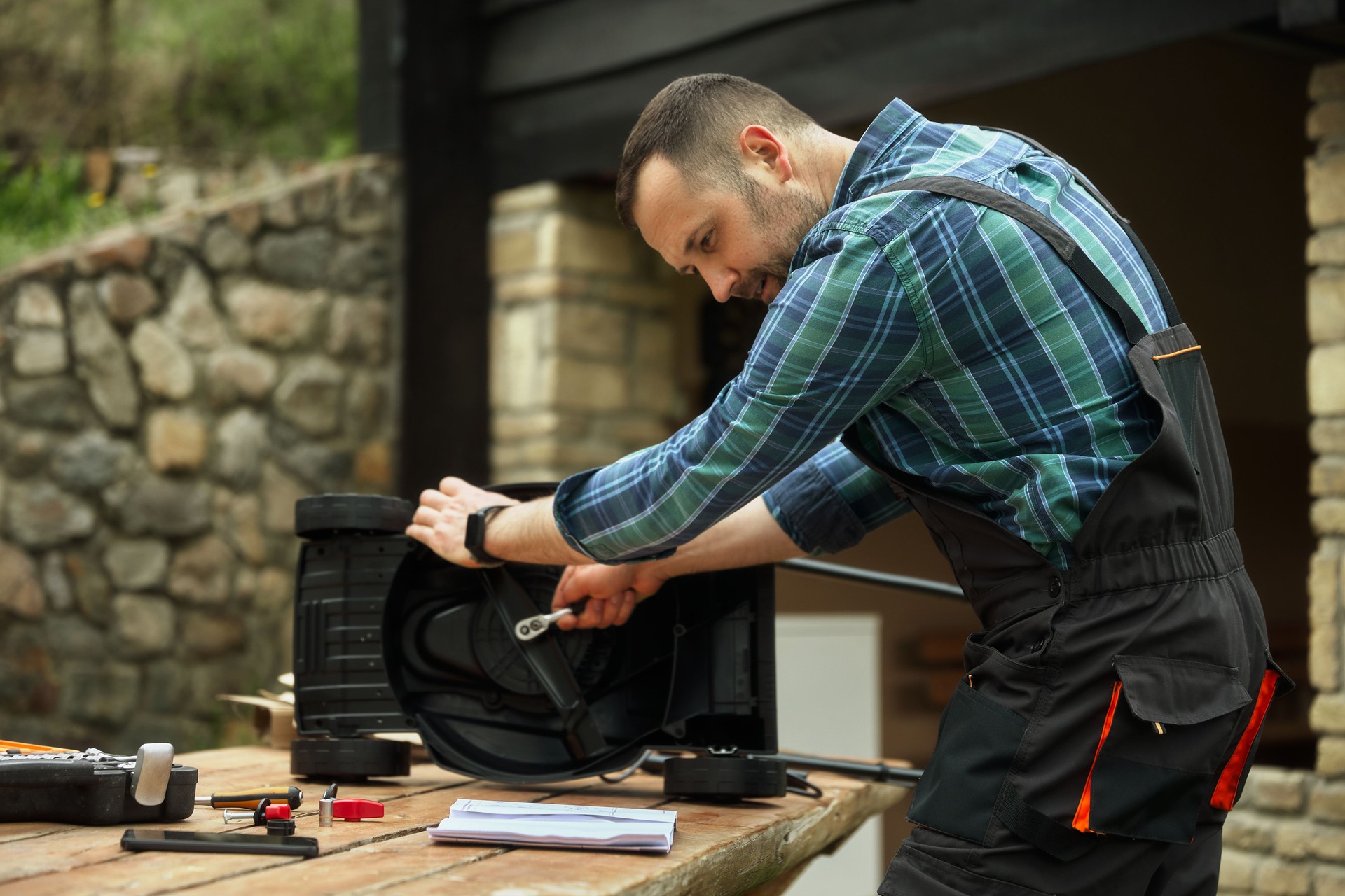Photo of a handsome middle-aged man dressed in a jumpsuit, assembling a new, unboxed lawn mower for his yard.